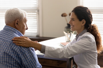 Smiling caring young female doctor support unhealthy elderly male patient in private hospital or...