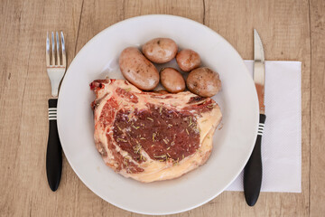 Raw and seasoned black angus steak with potatoes on a white plate. Concept meat, food, organic.