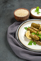 bottom view azerbaijani cuisine dolma in grape leaves on white plate bowls with natural yogurt rice a purple kitchen towel on dark background