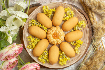 close up shot of a plate of cookies on wooden platter and flowers around it on marble ground