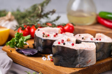 Fresh organic seafood. Raw sturgeon steaks on a cutting Board with spices and vegetables. On a gray background. Side view