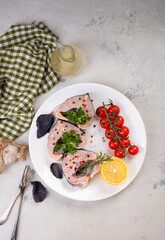 Fresh organic seafood. Raw sturgeon steaks on a white plate with spices and vegetables. On a gray background. Side view