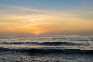 sunset over the ocean with colorful sky and large waves rolling in towards the coast