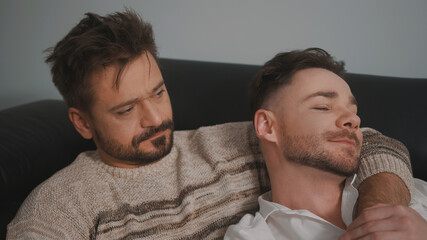 Fototapeta premium Young romantic gay couple spending day cuddling and relaxing on the couch. Different family lifestyle concept. High quality photo