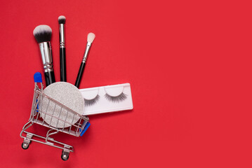 Creative concept with shopping trolley with makeup on a red background. brushes, mascara, false eye lashes