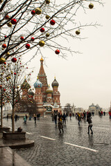 view of St. Basil's Cathedral on red square and bare trees with Christmas balls and walking tourists on a cloudy winter day in Moscow Russia