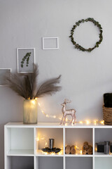 Details of the decorated New Year's Scandinavian interior. Shelving decor for Christmas. Garland, candles, deer, eucalyptus wreath, lights.