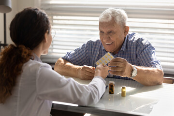 Obraz premium Back view of female doctor give pills medication to smiling mature male patient in private hospital. Woman GP or nurse recommend treatment, offer drugs medicines to happy elderly man client in clinic.