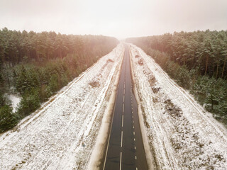 Empty road in the middle of the forest on a snowy winter day, view from a drone
