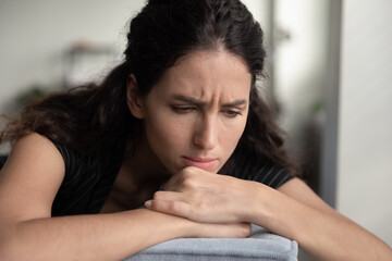 Close up of unhappy young Caucasian woman sit on sofa at home thinking feel depressed lonely at...