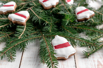 spruce branches and cookies shaped bell ring with red glaze on a white wooden background. concept of new year celebration with beautiful blurred bokeh