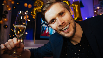 Celebrating Virtual Christmas New Year's Eve party 2021 at home during Covid-19 pandemic. Man holding and toasting champagne glasse How to celebrate and decorate foiled balloons of 2021.