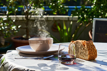 Table with hot dish of soup, bread and red wine at terrace