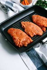 Marinated turkey steak with spices in a black grill pan on the table.