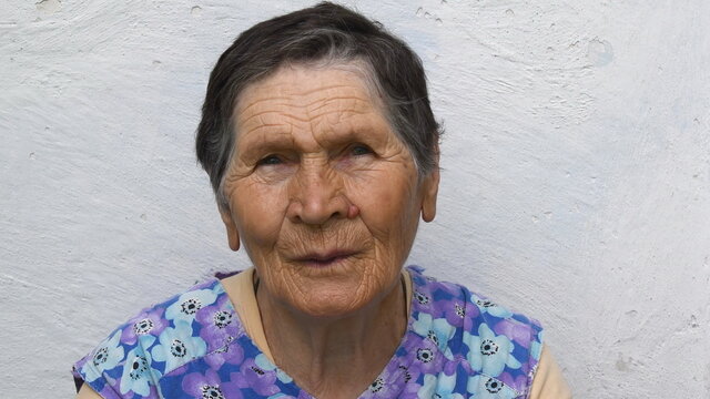 Authentic portrait of 80 years old lady of mixed ethnicity. Wrinkled face of elderly woman with concerned emotion and suspicious sight. Senior people real life