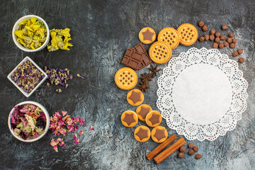 crescent shaped layout of sweets and bowls of dry flowers and a piece of white lace on grey ground