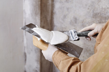 Construction worker with trowel and putty knife plastering a wall. House renovation concept. 