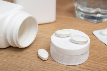 White pills of antibiotic, painkiller, vitamin supplements, zinc on wooden table, close-up view