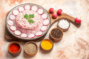 Obraz na płótnie Canvas Side view of delicious chicken salad with beet on a gray plate on wooden cutting board and radishes with different spices on mixed color background
