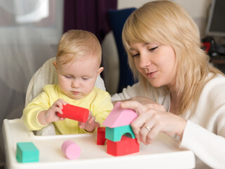 Obraz na płótnie Canvas Mom and baby play together with multi-colored constructor and build a pyramid. Home education and development