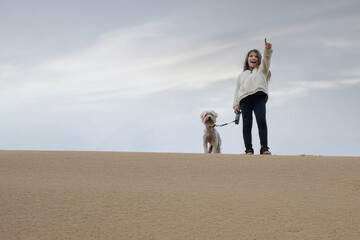 cute young girl running in the dunes with her dog in autumn