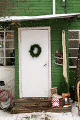 Winter country house is decorated with a garland for Christmas. There is a spruce wreath on the door, Christmas decorations on the steps. Decorate your home for the holiday. Christmas in nature.