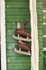 Brown vintage vintage skates hang on the green wooden wall of the house decorated with garlands. Decorate your home for the holiday. Christmas in nature. Ice skating in winter.