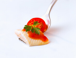 Herring fish fillet on a fork with herbs and tomato sauce. Isolated on white background