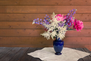 Beautiful bouquet made of astilbe, lupine and peonies in blue vase on rustic wooden table