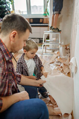 Father with kid repairing room together and unhanging wallpaper together