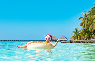 cute boy in a Santa hat on an inflatable donut in the ocean having fun and gives a thumbs up, the concept of Christmas and New year in exotic tropical countries and travel