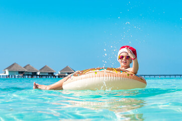 cute boy in a Santa hat on an inflatable donut in the ocean having fun and gives a thumbs up, the concept of Christmas and New year in exotic tropical countries and travel