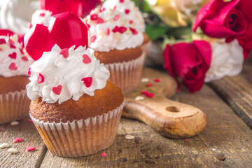 Fototapeta na wymiar Cupcake with Heart for Valentines. Valentine Day Sweet Dessert, vanilla cupcakes with whipped vanilla cream and red sugar hearts decor for Valentine's Day, wooden background with rose flowers bouquet