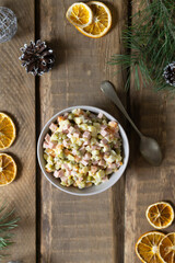 Traditional Olivier salad russian in a bowl with a spoon on a wooden background. Festive Russian cuisine. Top view. Copy space. Rustic style.