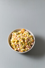 Olivier salad russian in a bowl on a gray background. Traditional Russian cuisine. Copy space. Vertical orientation.