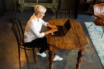 beautiful stylish woman aged in glasses at the table with a laptop