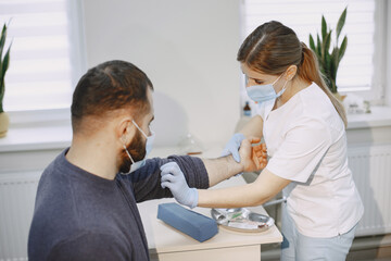 Skillful nurse is doing blood test for man in clinic. Man in a medical mask.