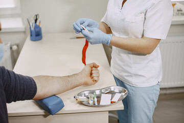 Skillful nurse is doing blood test for man in clinic. Man in a medical mask.