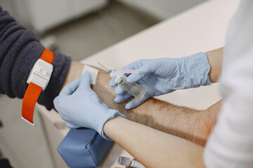 Skillful nurse is doing blood test for man in clinic. Man in a medical mask.