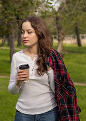 Girl in the park with a cup of coffee, plaid shirt on the shoulder