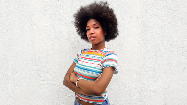African American teenage girl standing with arms crossed in front of a white wall. copy space