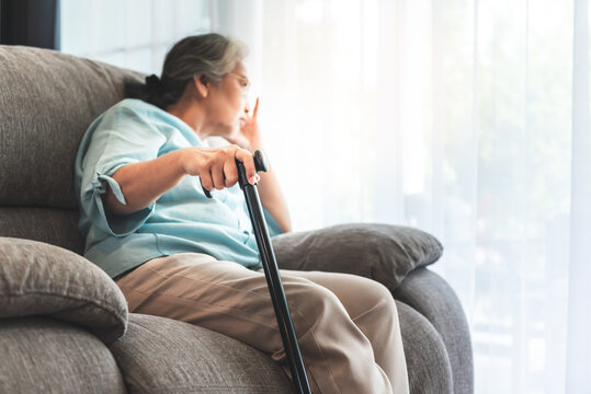 Close up images, Hand of Asian elderly woman Which holds the cane to support, Sitting absent lonely on the sofa and looking outside the door, to health care and retirement age concept.