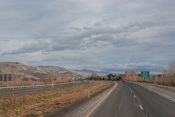 A beautiful landscape with a highway along which cars and trucks drive, on a sunny autumn day among the mountains, a blue sky with fluffy gray-blue clouds. Oregon, USA, 12-5-2019