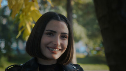 Young girl wooing her lover behind the tree. Smiling young cheerful woman with braces.