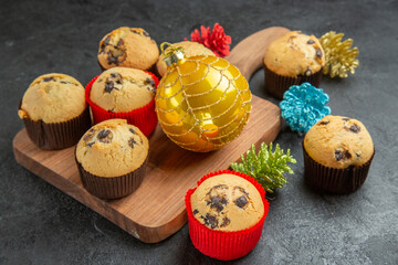 Side view of tea break with delicious small cupcakes and new year decorations on black background