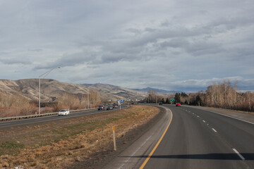 A beautiful landscape with a highway along which cars and trucks drive, on a sunny autumn day among the mountains, a blue sky with fluffy gray-blue clouds. Oregon, USA, 12-5-2019