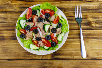 Tasty tuna salad with lettuce, black olives and fresh vegetables on wooden table. Top view