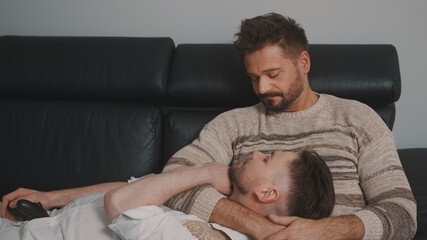 Lovers relaxing together on the couch. Handsome man resting his head on the lap of his husband. High quality photo