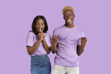Young African American couple screaming in excitement, making YES gesture over violet studio background