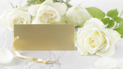 Obraz na płótnie Canvas White cream color roses flower with blank golden card on white stone background.